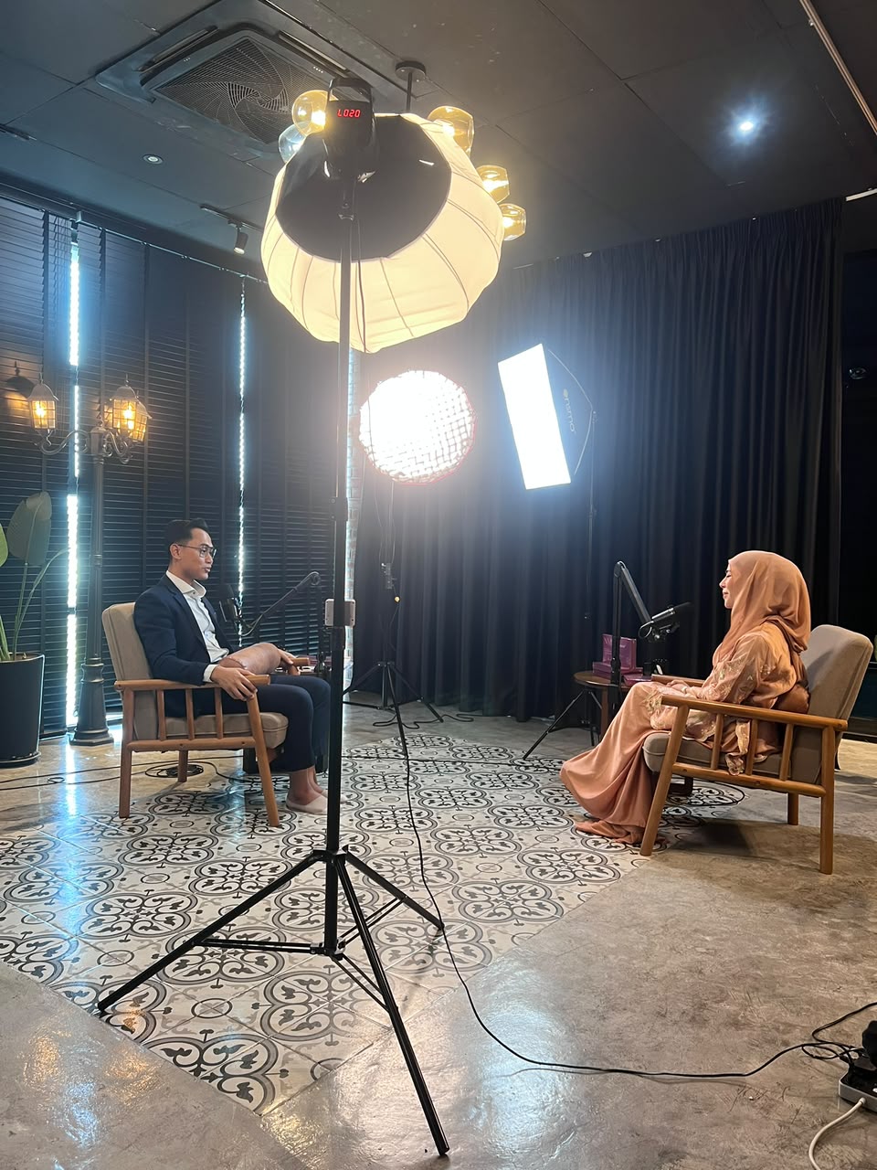 Madammu Eriyca Baiduri dalam sesi rakaman podcast di studio bersama panel, dengan suasana behind-the-scenes yang tenang dan profesional.